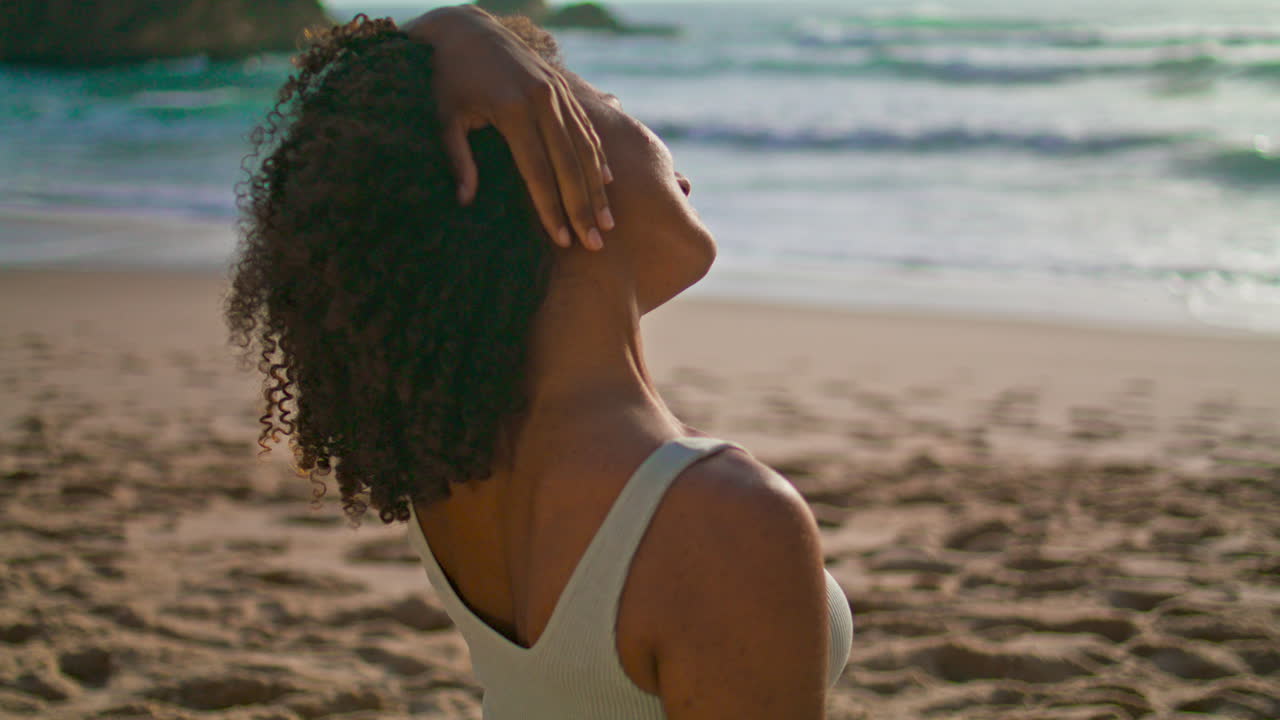 Ragazza africana che allunga il collo su una spiaggia sabbiosa, primo piano. Donna che si riscalda all'alba.