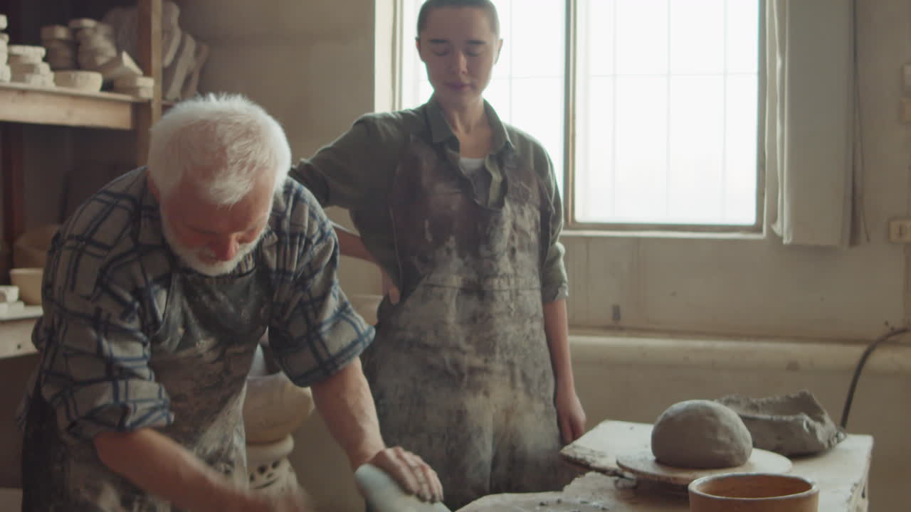 el alfarero mayor enseñando a la mujer joven a lanzar en la rueda