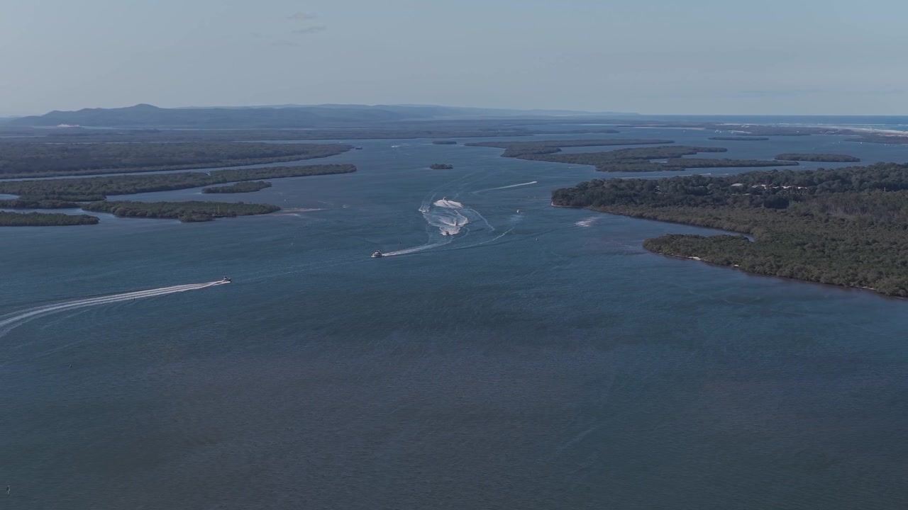 Perahu cepat menciptakan jejak gelombang di air yang tenang - Pulau George Collins dan Pulau Coomera di Australia. Foto udara.