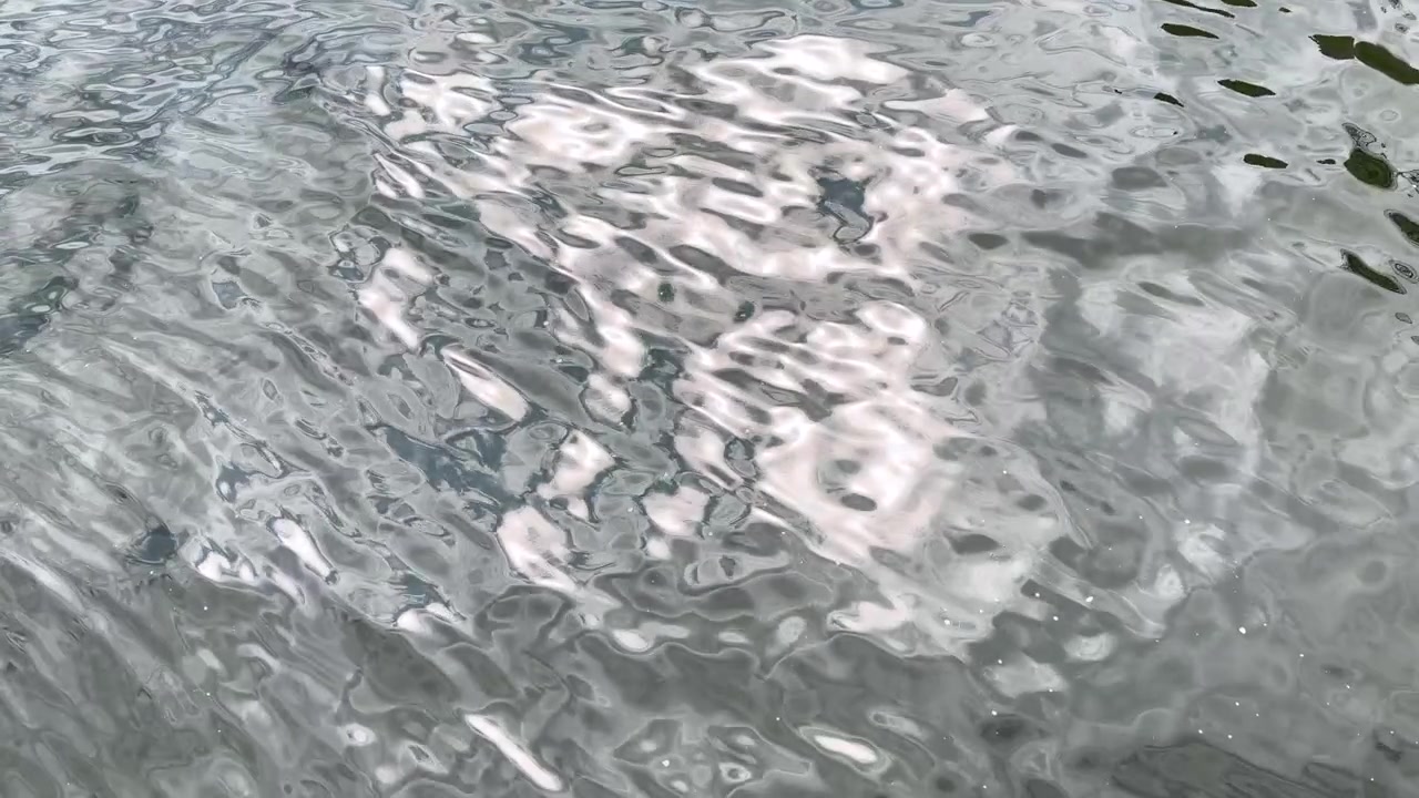 Suaves ondulaciones se mueven sobre una superficie de agua gris reflejando la luz brillante del sol en una toma estática.