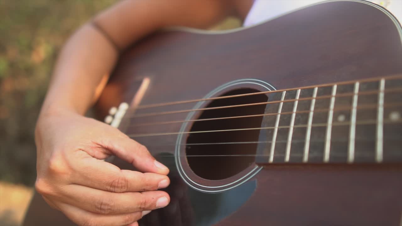 mano de una joven morena tocando las cuerdas de una guitarra marrón oscura