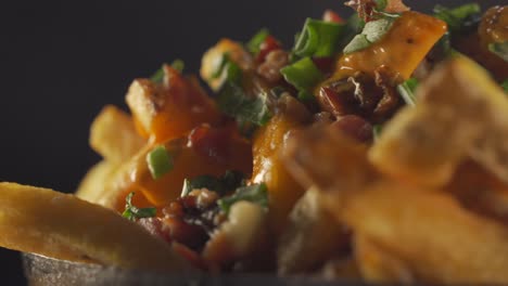 un primer plano estacionario de un tazón lleno de tocino y papas fritas cubierto con queso cheddar y cubierto con cebolletas