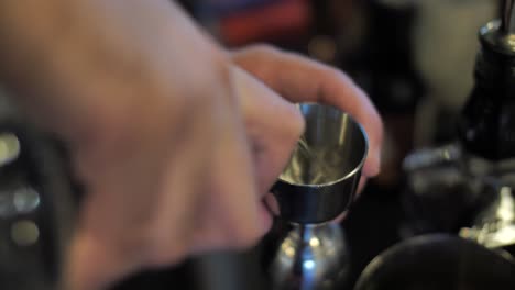 Preparing-alcohol-cocktail-pouring-vodka-into-measure-glass-on-bar-counter,-close-up