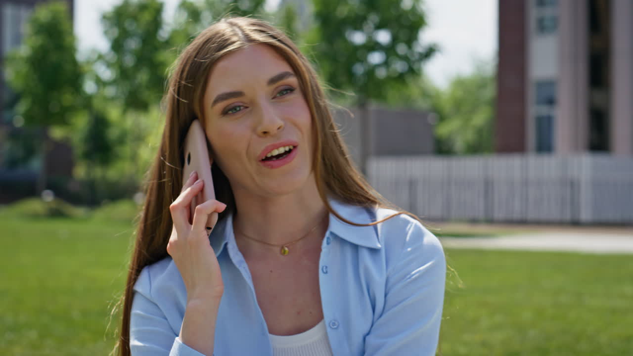 Joyful woman chatting mobile phone sitting green park lawn closeup. Smiling girl