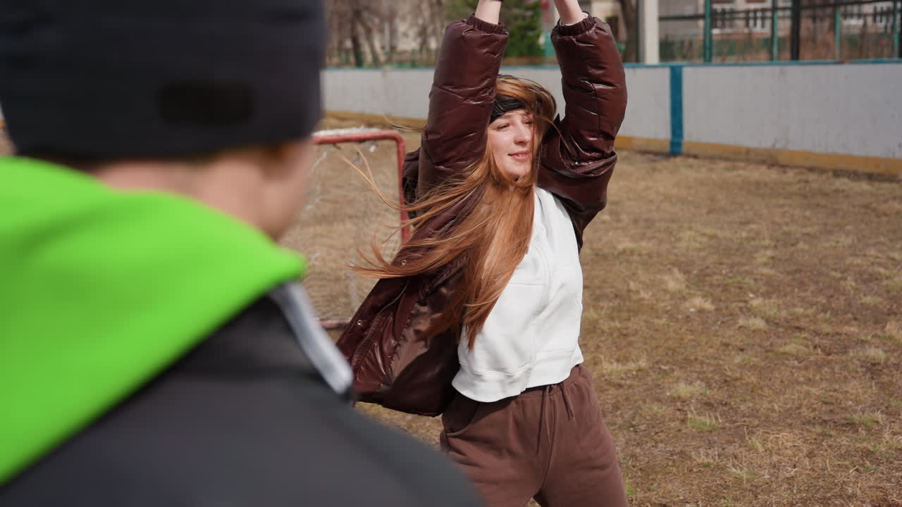 Una mujer alegre levanta los brazos, una jugadora feliz gesticula con entusiasmo cerca de un pequeño objetivo, una mujer llena de energía levanta las manos en señal de celebración junto a una modesta portería deportiva con un entrenador observando.