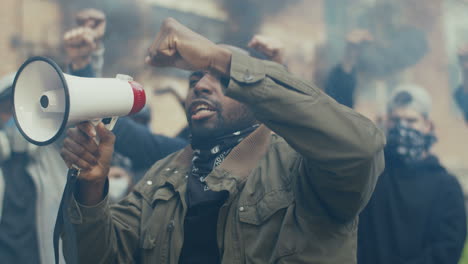 hombre afroamericano gritando en un altavoz en una protesta con un grupo multiétnico de personas en la calle