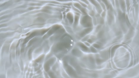 water splash. water drop creating ripple. pure water with reflections sunlight in slow motion. water surface texture top view. sun and shadows. clean swimming pool ripples and wave. 4k