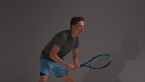 fotografía de estudio de un jugador de tenis masculino devolviendo el tiro en un partido golpeando la pelota con una raqueta contra un fondo gris 1