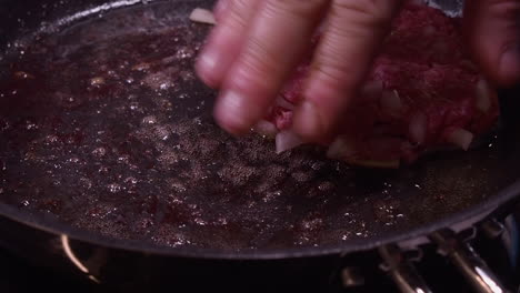 hombre caucásico usa la mano para aplanar hamburguesa cocinando en una sartén caliente