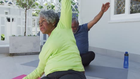 feliz pareja de ancianos afroamericanos practicando yoga en la alfombra en el patio