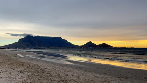 Atemberaubende-Kapstadt-Tafelberg-Strandlandschaft,-Goldgelb-orangefarbener-Sonnenuntergang,-Südafrika-Vogel,-Wegfliegende-Möwe,-Ebbe,-Unglaubliche-Küstenlinie,-Himmel-In-Zeitlupe,-Schwenk-Nach-Rechts