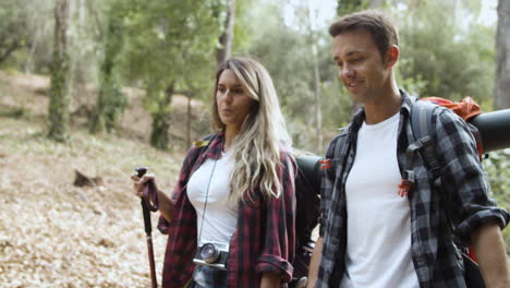 couple of active tourists carrying camping backpacks and talking on the woods