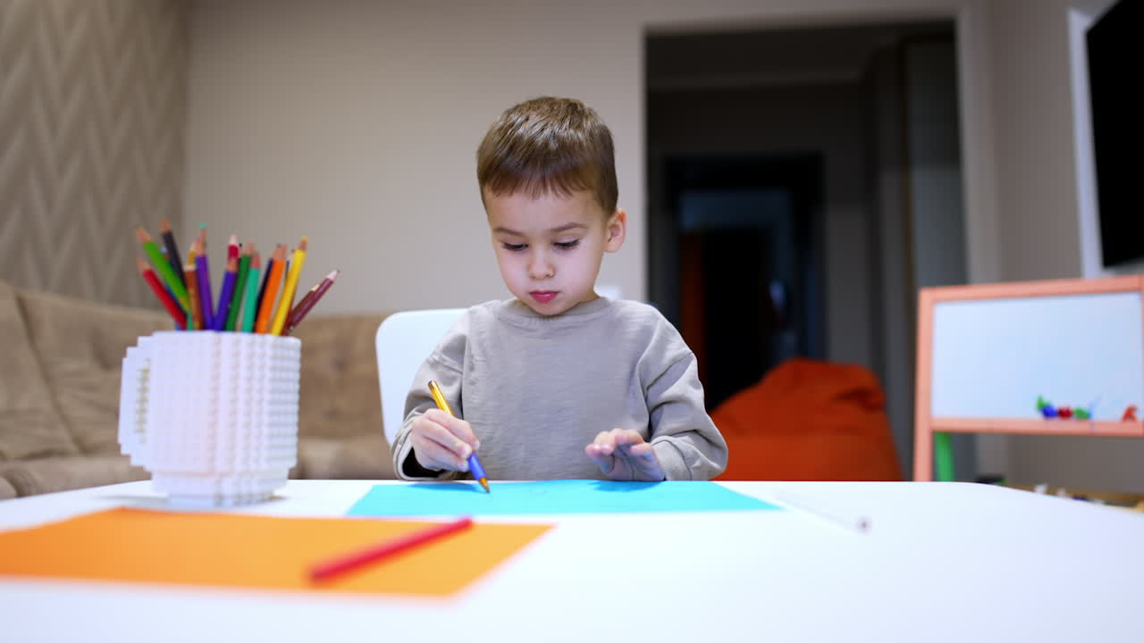 Child drawing creatively. A young boy sits at a table, focusing on drawing with colored pencils and markers, surrounded by art supplies