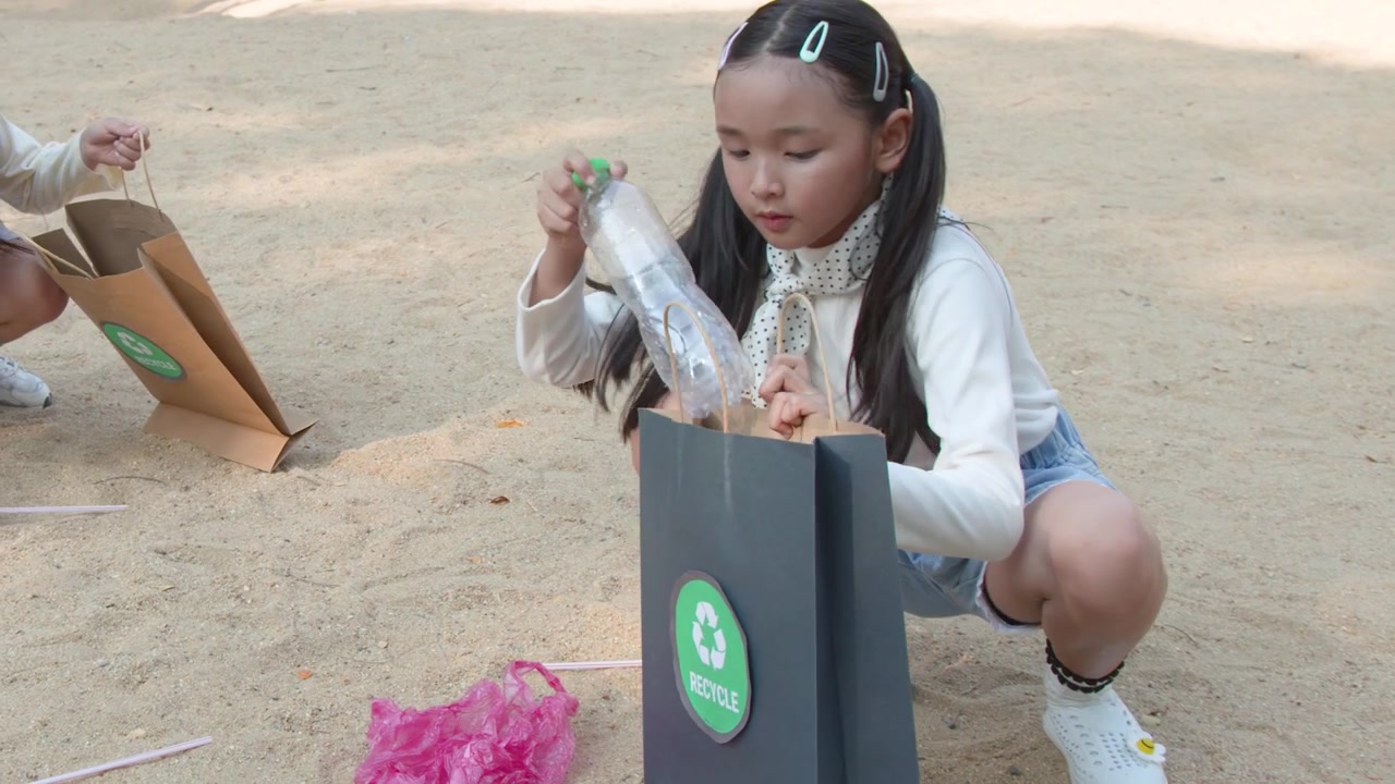 Giovane ragazza thailandese raccoglie rifiuti di plastica e li ripone in sacchi per la raccolta differenziata all'aperto.