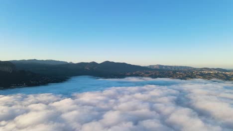 aerial pan of sea of clouds over calpe, spain, as the fog rolls over the landscape, creating a dreamlike scene