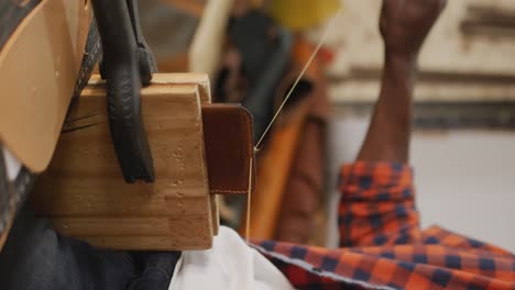 Hands-of-african-american-craftsman-using-tools,-preparing-wallet-in-leather-workshop