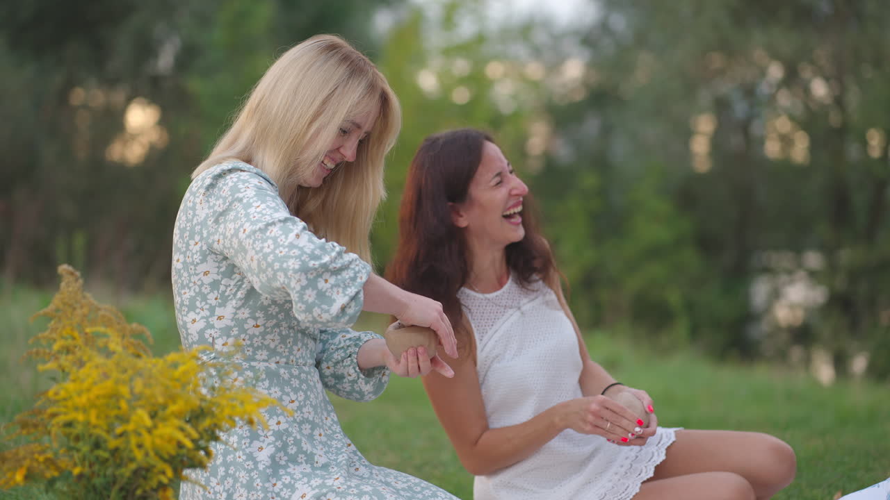Laughing young women sculpt clay products in nature in the park in the open space. Group creative classes women's circle communication humor fun spending time together.