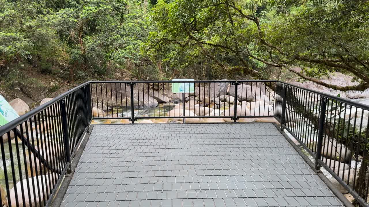 A serene walkway through lush tropical foliage leads to a scenic overlook of the Mossman River in Port Douglas, Australia