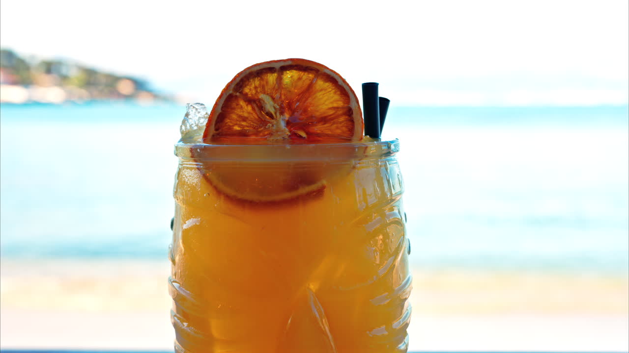 Close up of an orange cocktail on a table with a blurred view of the sea on the background