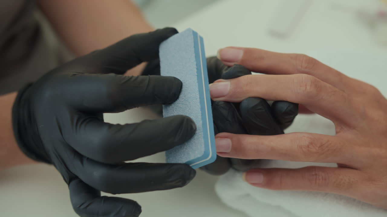 Gloved Hands of Nail Technician Polishing Nails of Client with File