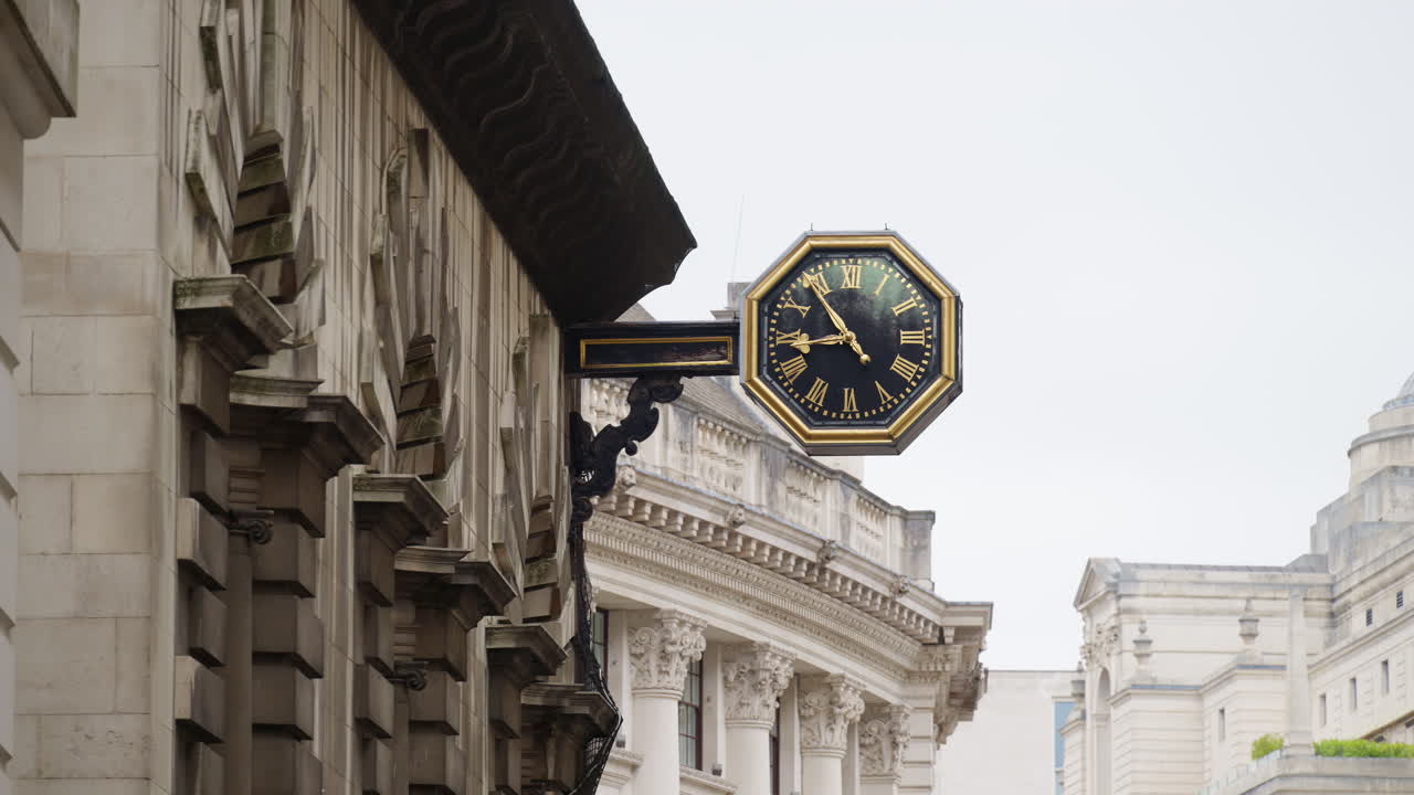 Close-up of a decorative black and gold clock mounted on a historic stone building in London, England