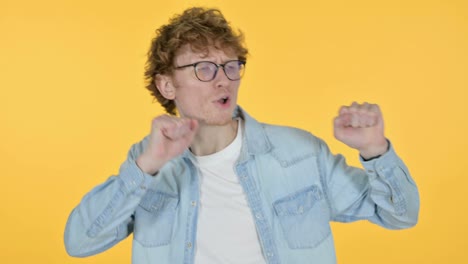 excited redhead young man dancing, yellow background