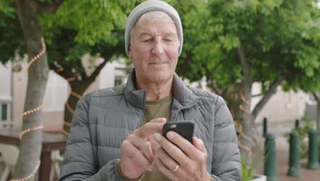 Retrato-De-Un-Anciano-Caucásico-Enviando-Mensajes-De-Texto-Navegando-Usando-Un-Teléfono-Inteligente-Sonriendo-Feliz-Disfrutando-De-La-Comunicación-Móvil-En-El-Fondo-Urbano-De-La-Ciudad