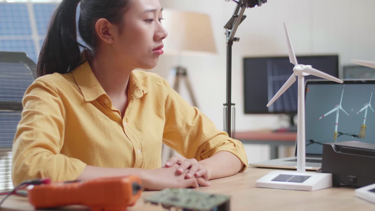사무실에서 태양전지 에 노트북으로 작업하는 동안 풍력 터빈을 테스트하는 데 실패하는 아시아 여성의 가까운 모습