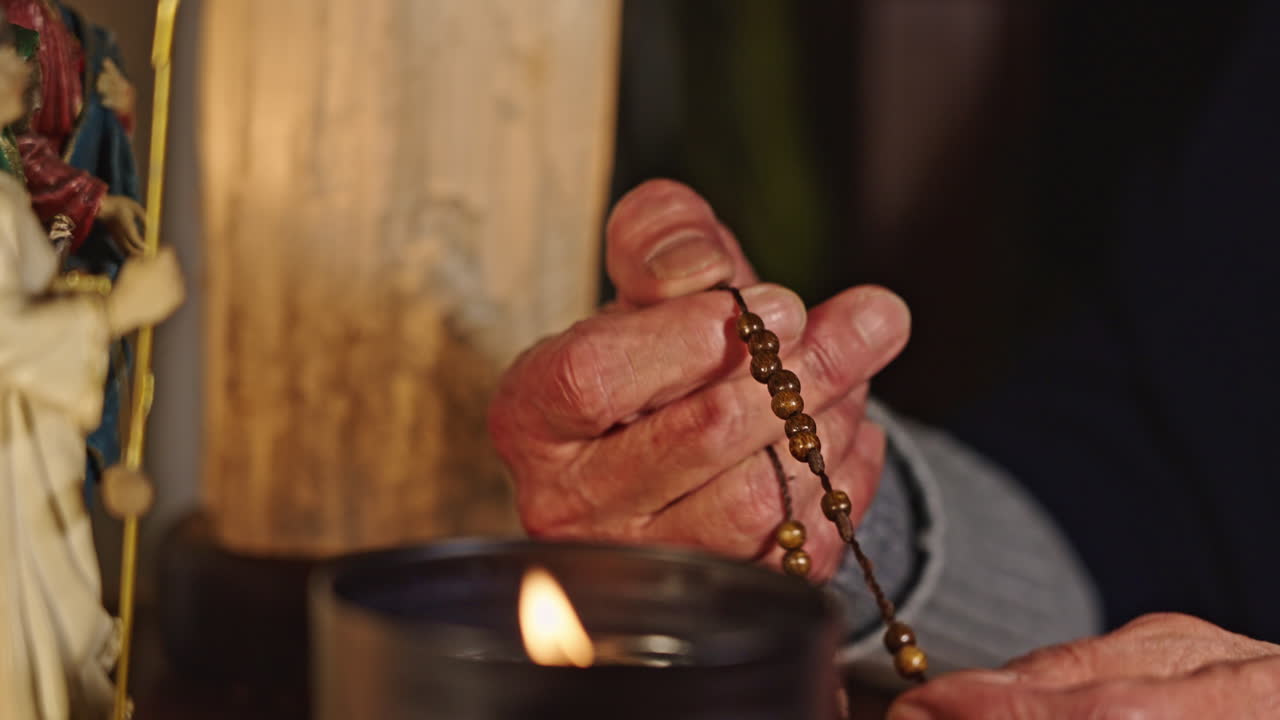 Elderly Person's Hands Praying with Rosary by Candlelight