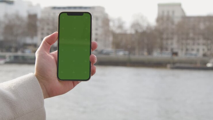 Close Up Of Man Holding Green Screen Mobile Phone Looking Out To River Thames And Embankment In London UK