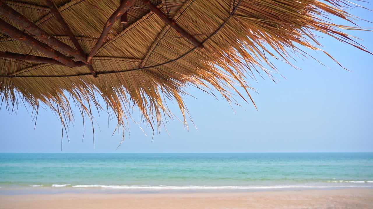 Ombrellone di paglia su spiaggia tropicale esotica con mare sullo sfondo