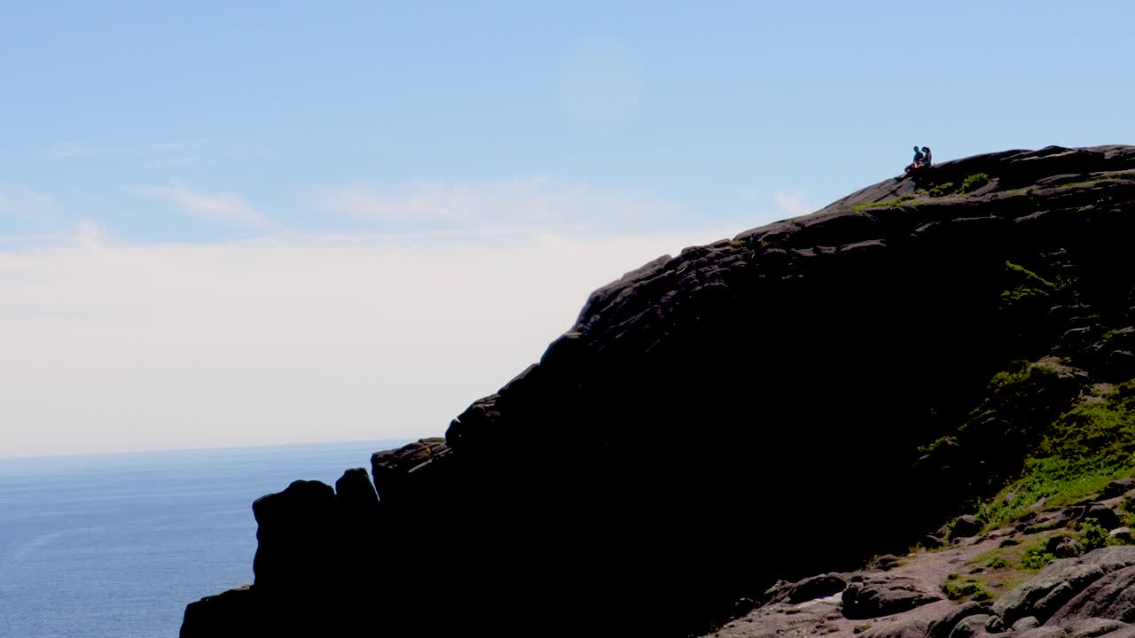 Panoramica lenta mentre gli escursionisti si rilassano su una scogliera rocciosa a picco sull'oceano.