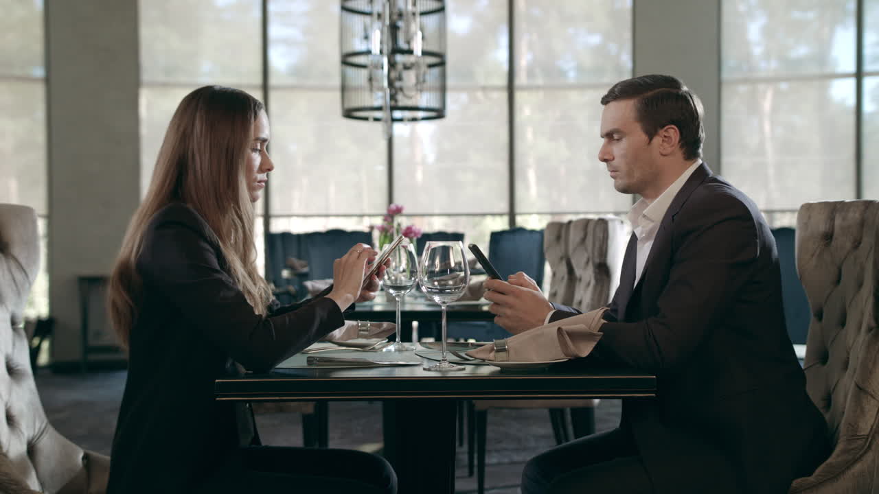 Persone d'affari che usano il cellulare al ristorante. Coppia d'affari che usa i telefoni.