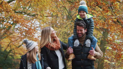smiling family walking along path through autumn countryside as father carries son on shoulders