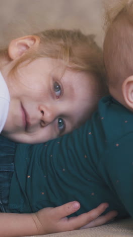 funny girl hugs little brother nibbling rubber teat of water bottle on large bed in spacious room extreme close view