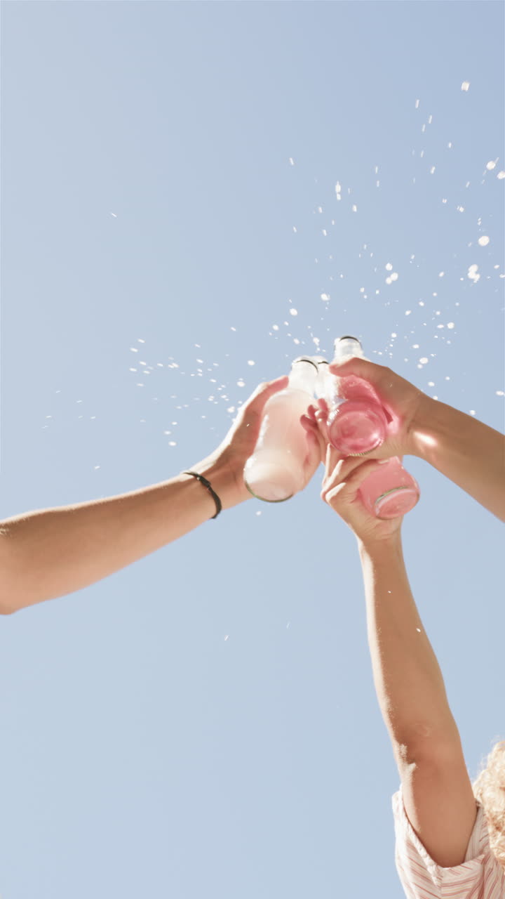 Vertical video: Cheers with drinks, friends toasting with bottles, celebrating together outdoors