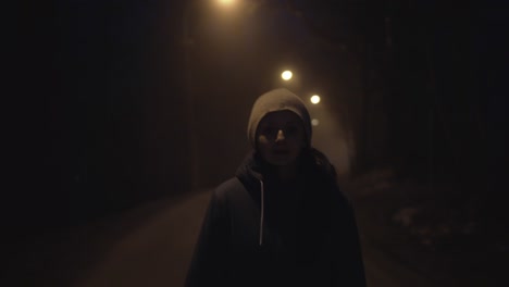 girl walking dark road in light of street lamps, face front view, looking into camera