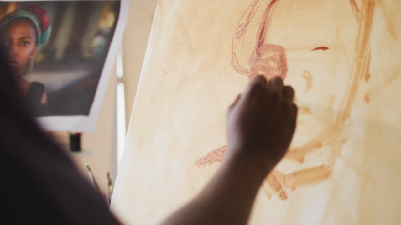 pintor afroamericano de sexo masculino pintando a partir de una fotografía en lienzo en el estudio del artista