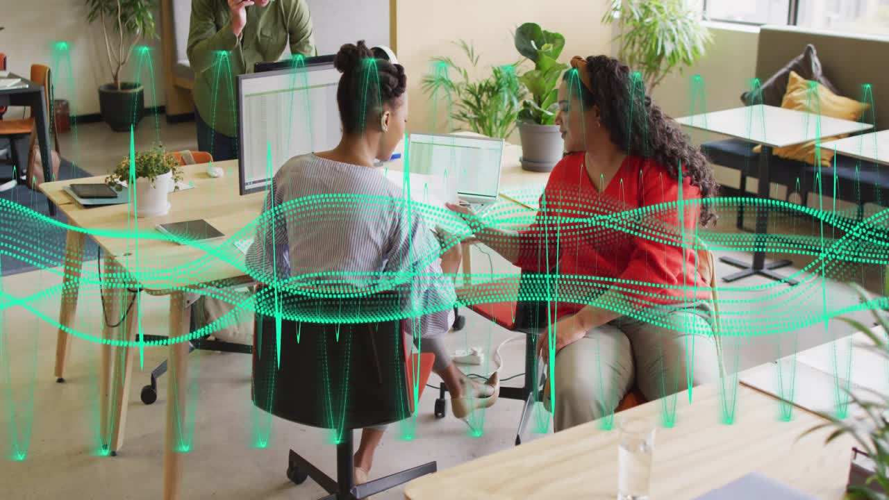 Woman in red handing paper, grey woman turning and reviewing on work laptop waveform pulsing across