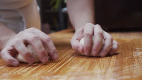 Chef-rounds-the-pizza-dough-parts-on-wooden-table