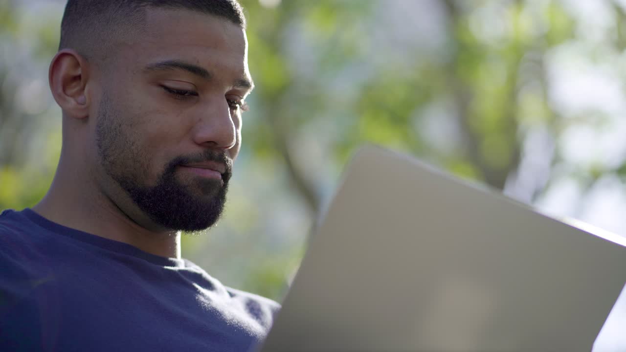 Bottom view of young man in park working on laptop, thinking