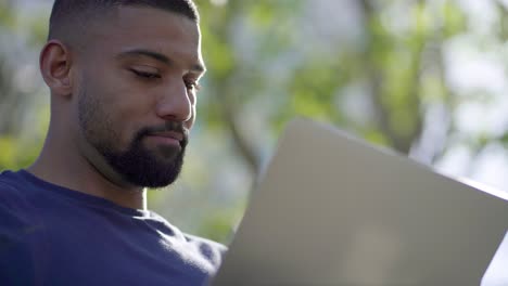 Bottom-view-of-young-man-in-park-working-on-laptop,-thinking