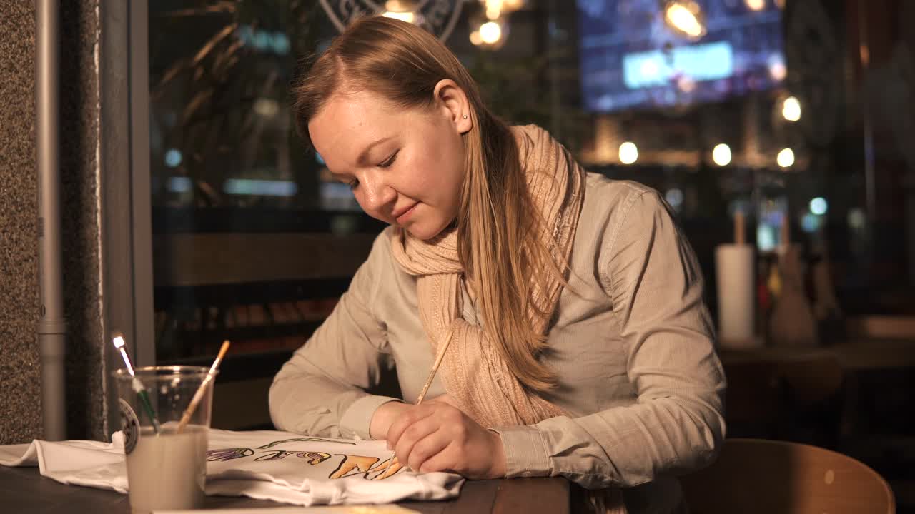 Woman painting a shirt in a cafe at night