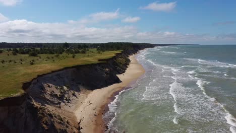 Flying-Over-Coastline-Baltic-Sea-Ulmale-Seashore-Bluffs-Near-Pavilosta,-Latvia-and-Landslides-With-an-Overgrown,-Rippling-Cave-dotted-Cliff-and-Pebbles
