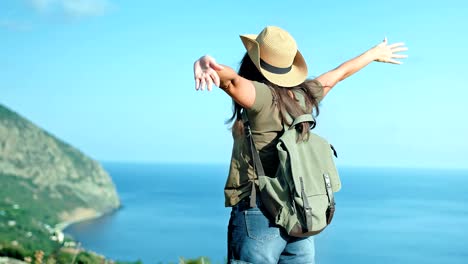 active backpacker woman traveler in hat and sunglasses enjoying amazing seascape raising hands