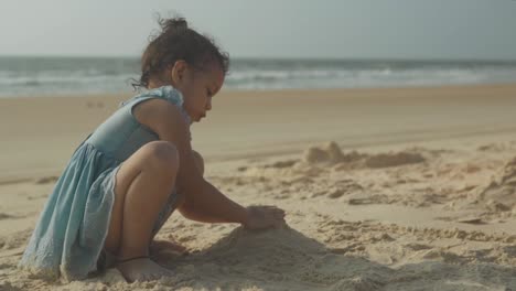 medium view of young toddler playing in sand at beach with ocean waves behind
