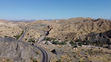 drone aéreo hacia adelante moviéndose disparó sobre coches y camiones moviéndose en un sinuoso camino rcd a través de balochistan en un día soleado