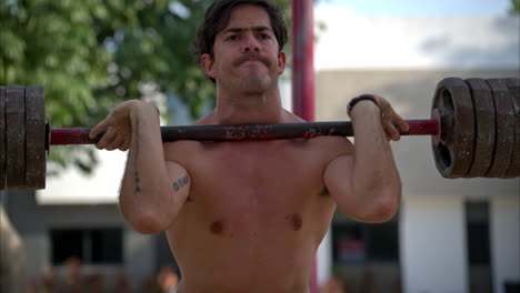 slow motion portrait of a latin male athlete performing a front squat with a bar at the fitness ground of the park on a sunny morning