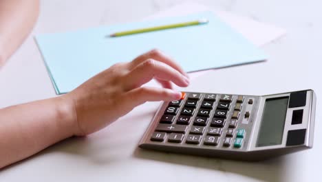 la mano cerrada de una mujer está usando una calculadora para calcular y anotar sus gastos contables mensuales en casa.