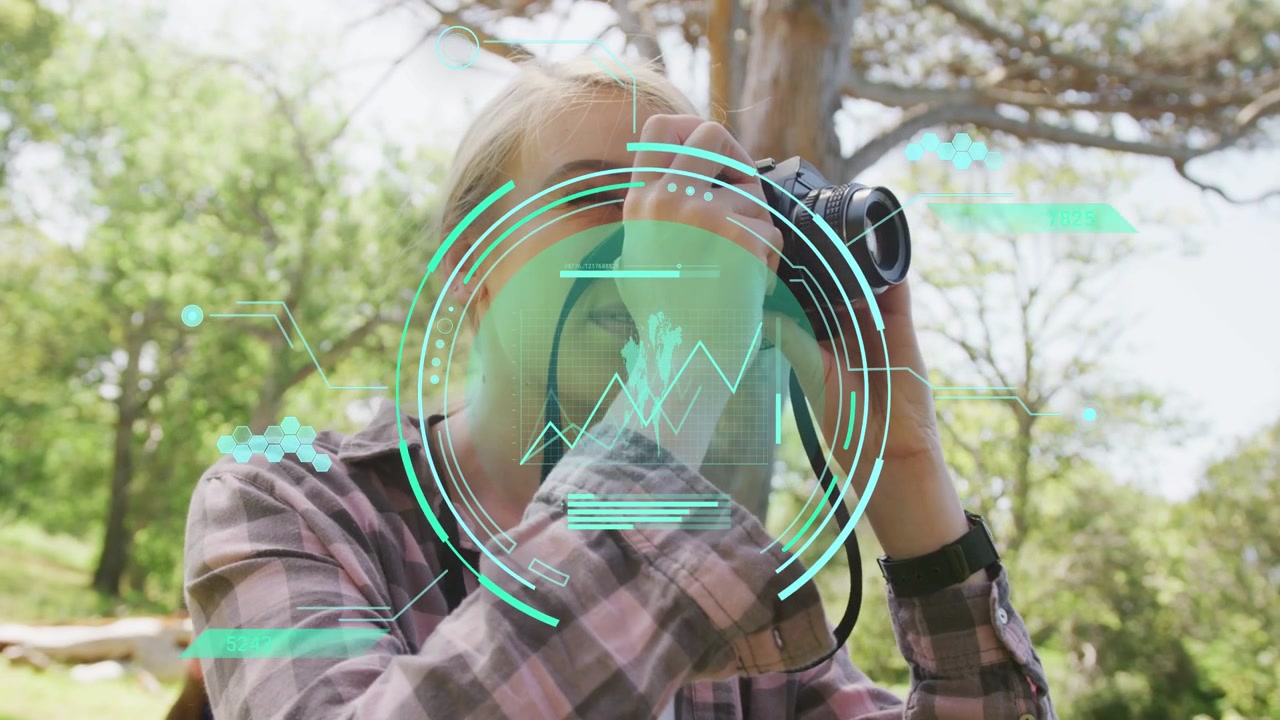 Woman lifting camera from chest and composing shot in woods for tech, teal HUD showing maps